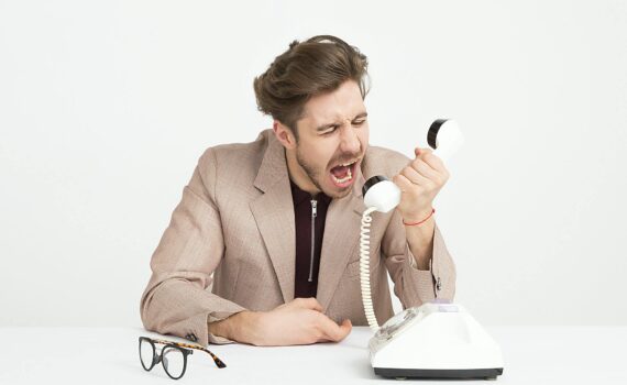 man wearing brown suit jacket mocking on white telephone